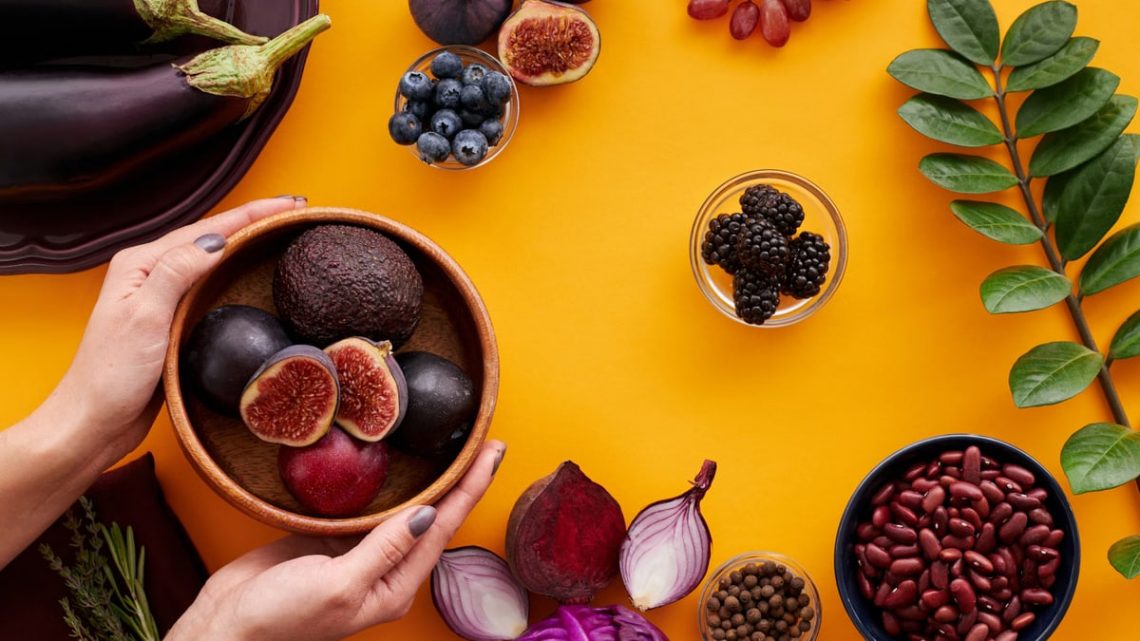 Colorful arrangement of fruits and vegetables on a yellow background, featuring figs and eggplants.